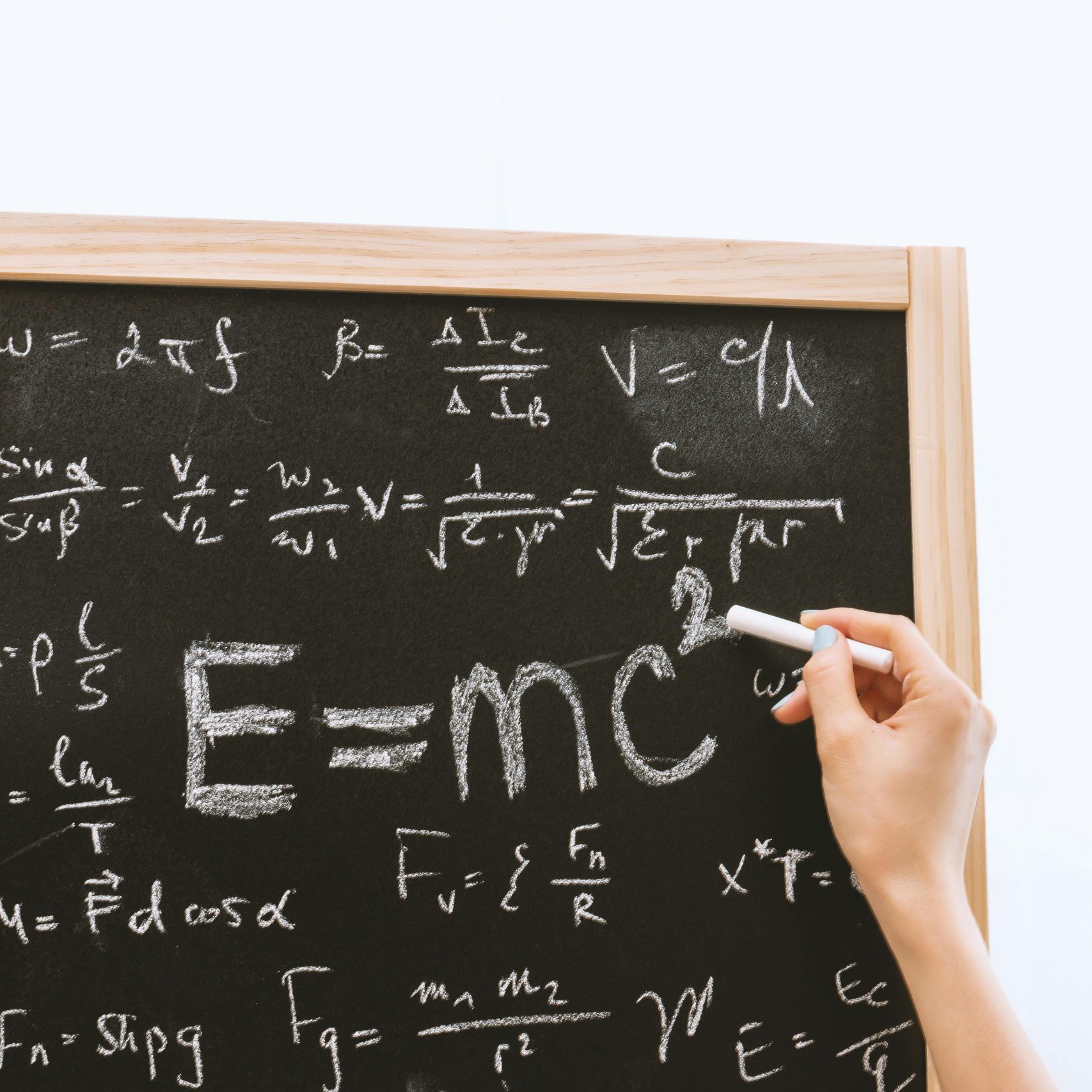 Close-up of hand writing physics equations on a chalkboard indoors.