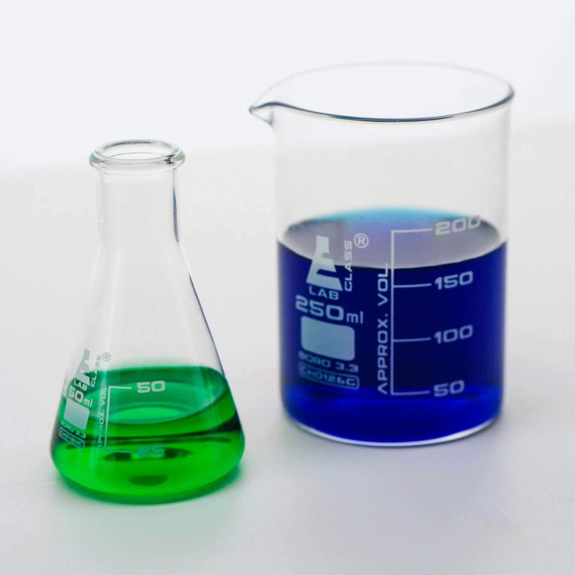 Close-up of beakers filled with vibrant green and blue liquids in a laboratory setting.
